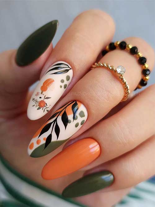 Long olive green and burnt orange nails with two light beige accent nails adorned with abstract nail art and black autumn leaves.