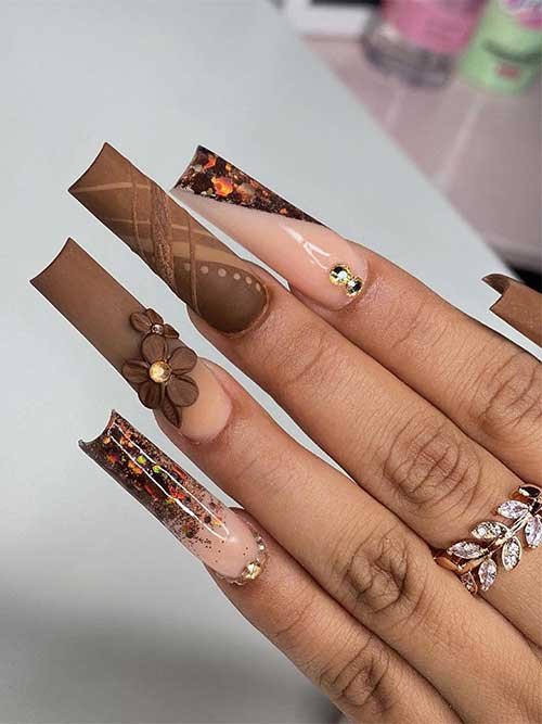Long square-shaped matte brown Thanksgiving Nails with two nude accent nails adorned with different autumnal glitter