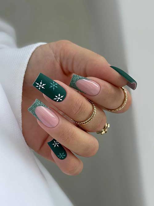 Long square-shaped matte dark green nails with white and light green snowflakes and two accent glitter green French tip nails