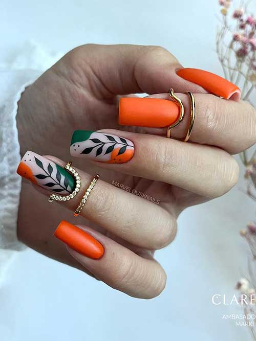 Long vibrant burnt orange nails with two nude accent nails adorned with green and orange abstract nail art and black leaves