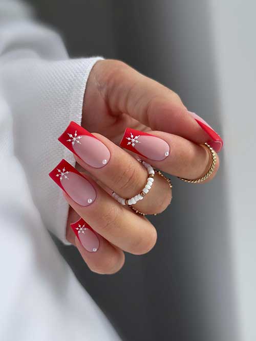 Matte red French tip nails with a white snowflake on each nail tip and a white pearl above each cuticle