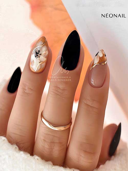 Medium almond matte black nails with two accent flower nails adorned with gold swirl nail art