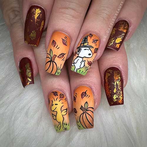 Medium coffin Thanksgiving nails 2023 feature matte burgundy nails with gold foil patches, and two yellow-orange accent nails