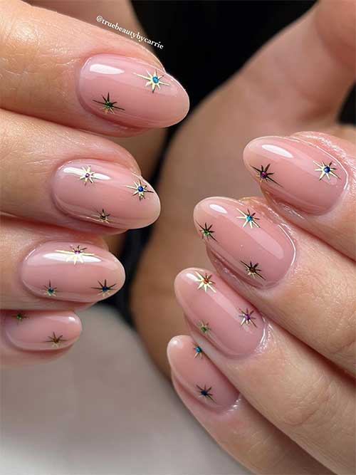 Nude nails almond almond-shaped with chrome gold stars adorned with a dot in their centers using different chrome colors