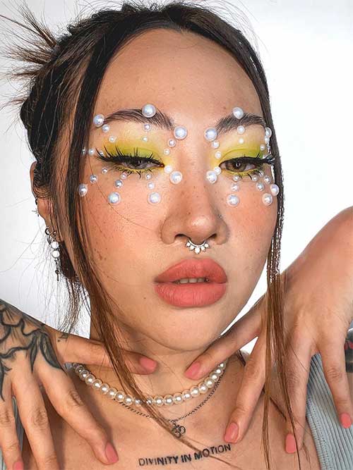 Pastel yellow and green eyes look adorned with white pearls forming a big snowflake on each eye, and nude pink lips