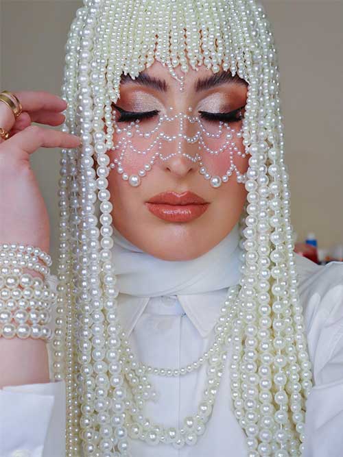 Pearl eyeshadow look with nude lips and pearl decoration on cheeks and nose, pearl headpiece, and pearl bracelet