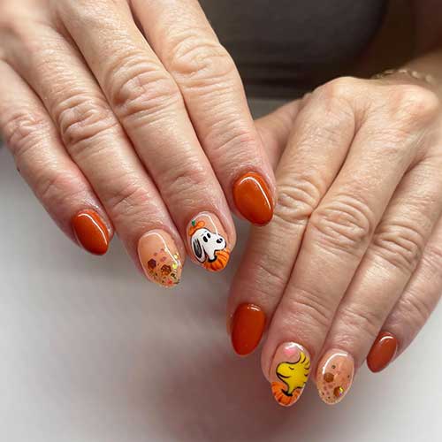 Short burnt orange Thanksgiving Nails with two accent nude nails feature glitter and snoopy dog and Woodstock inside pumpkins