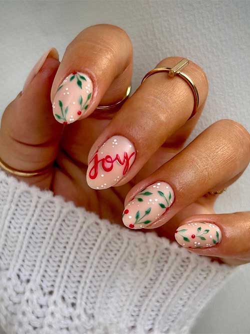 Short nude Christmas holly nails feature green leaf sets with a big red dot, white dots, and a JOY word on an accent nail