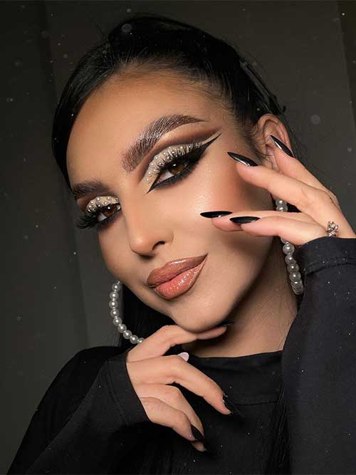 Smokey cut crease look and glam glitter eyeshadow adorned with white pearls, nude glossy lips, and black nails.