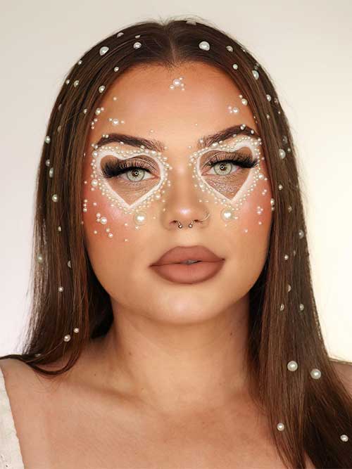 Valentine’s pearly makeup look features shimmer eyeshadow, a big white heart around each eye, and adorned with white pearls