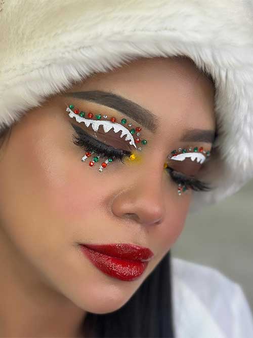 Creative gingerbread icicle eye makeup look with red and green rhinestones over matte brown eyeshadow. And glossy red lips