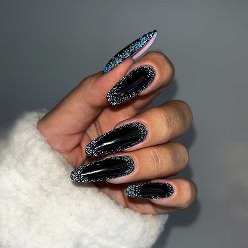 Long almond-shaped glossy black New Year’s nails with silver glitter on the nail perimeter.