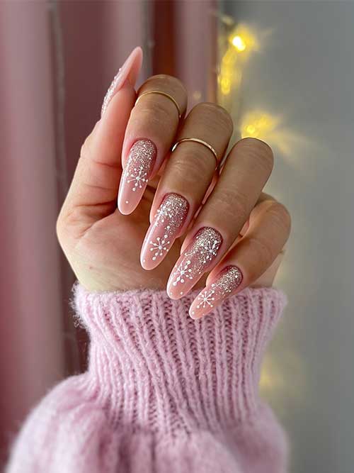 Long almond shaped nude Christmas nail design with white snowflakes and gold glitter above the cuticles
