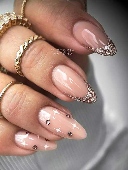 Long almond shaped rose gold glitter French New Year’s nails with two accent nude nails adorned with rhinestones and white stars. Long almond shaped rose gold glitter French New Year’s nails with two accent nude nails adorned with rhinestones and white stars.
