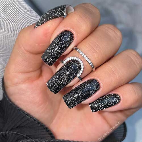 Long square-shaped sparkling black New Year’s nails 2024 with shimmering silver glitter.