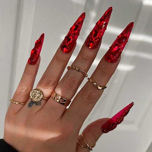 Long stiletto red New Years nails adorned with big and small red rhinestones