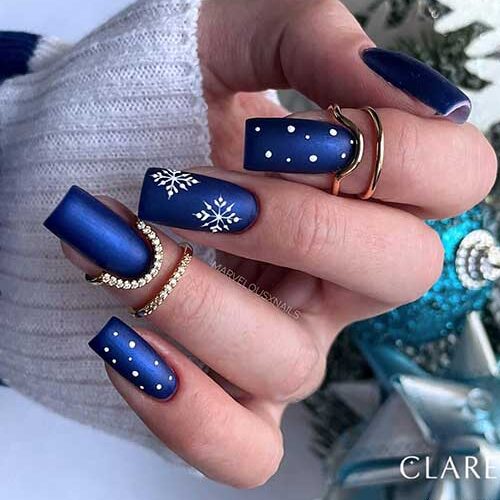 Medium square-shaped navy blue winter nails with an accent adorned with white snowflakes, and two accent white dots nails