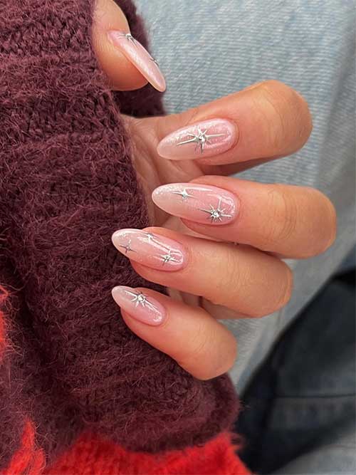 Shimmering long almond-shaped nude pink New Year's Eve nails with metallic silver stars some of them adorned with a crystal Shimmering long almond-shaped nude pink New Year's Eve nails with metallic silver stars some of them adorned with a crystal