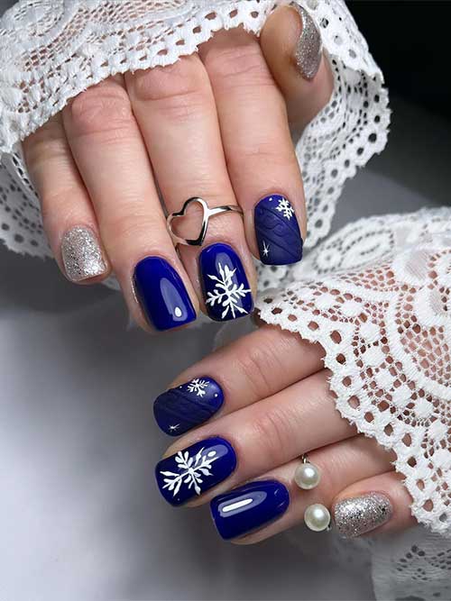 Short glossy navy blue winter nails with snowflakes, sweater nail art on an accent nail, and two silver glitter accent nails