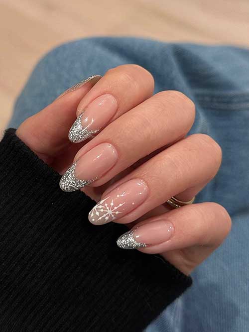 Silver glitter French New Year’s Eve nails with an accent nude nail adorned with white snowflakes on the nail tip