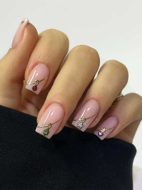 Simple Christmas nails with nude base color feature gold swirls creating diagonal French tips with dangle Christmas motifs