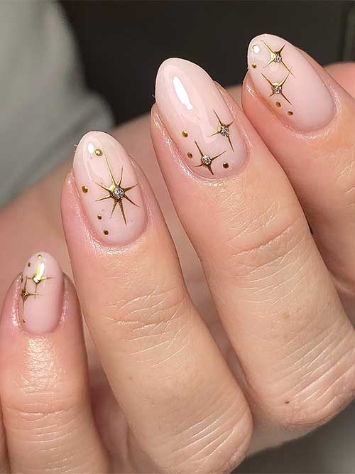 Simple nude Christmas nails with gold dots and stars adorned with silver glitter in their centers 