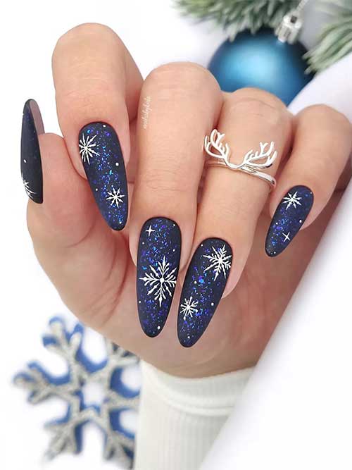 Stunning very dark navy blue winter nails adorned with white snowflakes and blue flakes