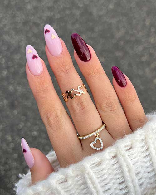 Long almond light pink Valentine’s nails adorned with light yellow and dark red hearts besides two accent dark red nails