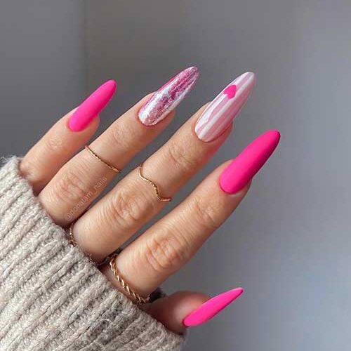 Long almond-shaped neon pink Valentine’s nails with a nude pink accent nail adorned with white stripes and a red heart