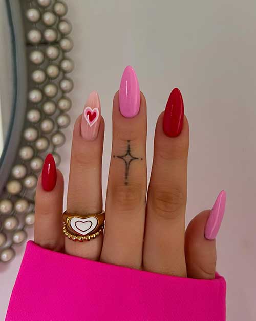 Long almond-shaped pink and red Valentine’s nails with an accent nude nail adorned with a heart shape