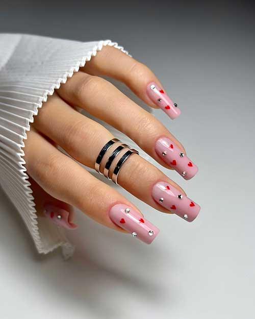 Long square-shaped nude Valentine’s nails with tiny red hearts and silver rhinestones