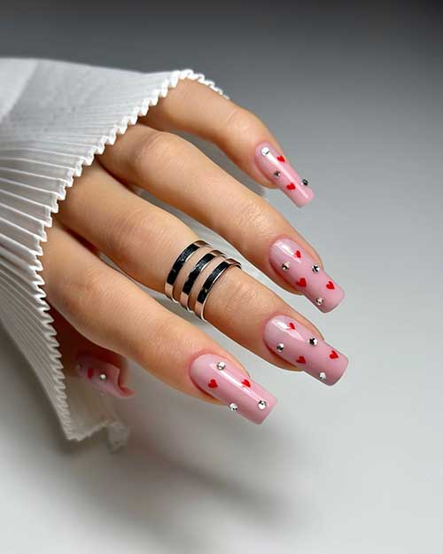 Long square-shaped nude Valentine’s nails with tiny red hearts and silver rhinestones Long square-shaped nude Valentine’s nails with tiny red hearts and silver rhinestones
