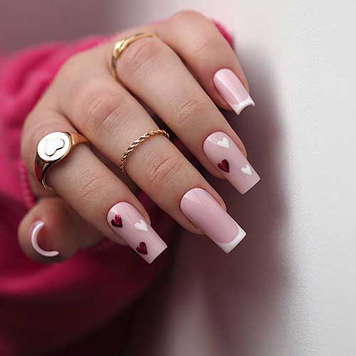 Long square-shaped white French tip nails with two accent nude nails adorned with red and white heart shapes