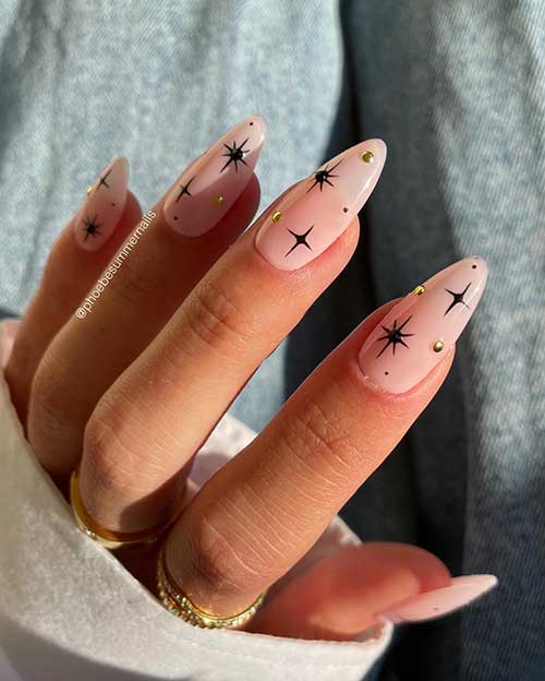 Nude nails almond-shaped and adorned with black stars and little gold rhinestones are one of the best winter nail art designs