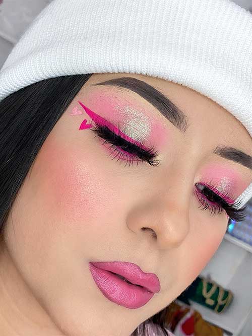 Pink Valentine’s Day makeup look features light pink eyeshadow, hot pink winged eyeliner, heart shapes, and pink lips