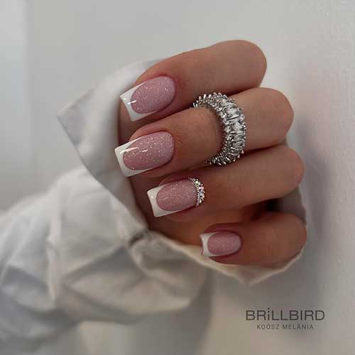 Shimmer White French tip nails over glittering nude base color. Besides, some silver rhinestones on an accent nail