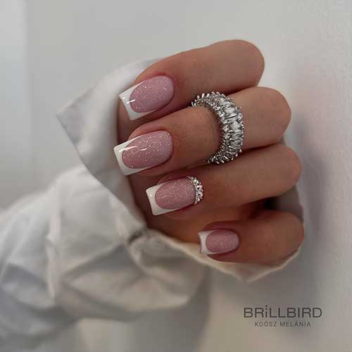 Shimmer White French tip nails over glittering nude base color. Besides, some silver rhinestones on an accent nail Shimmer White French tip nails over glittering nude base color. Besides, some silver rhinestones on an accent nail