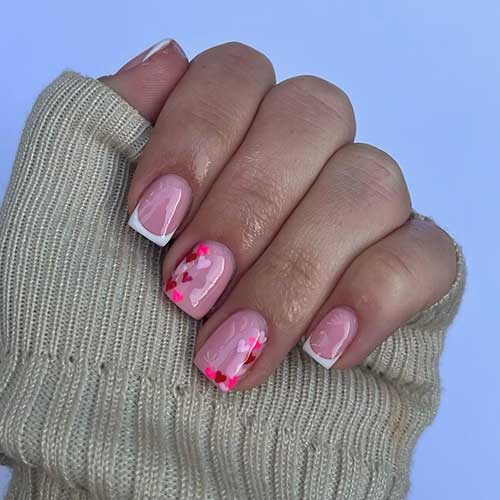 Short Valentine’s Day nails with white French tips and two nude accent nails adorned with tiny heart shapes