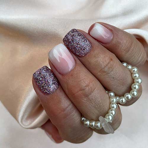 Short baby boomer nails with two accent dark purple nails adorned with sparkling multicolored glitter