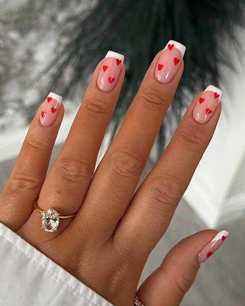 Simple short white French manicure over a nude base color and adorned with tiny red heart shapes