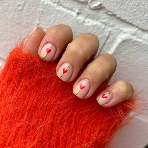 Stylish short nude Valentine's nails adorned with a gold centerline and a red heart shape on the center of each nail Stylish short nude Valentine's nails adorned with a gold centerline and a red heart shape on the center of each nail
