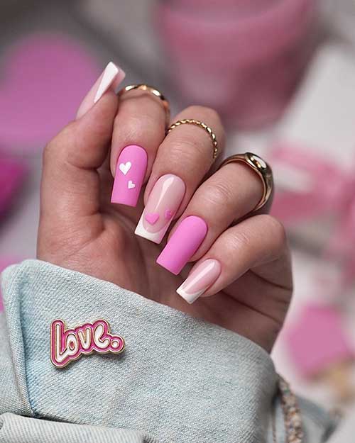 White French tip nails with two accent matte candy pink nails, one adorned with two white heart shapes