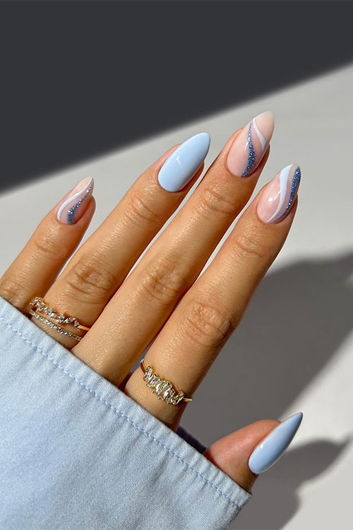 Almond-shaped light blue and glitter blue swirl nails over nude base color besides, two accent light blue nails Almond-shaped light blue and glitter blue swirl nails over nude base color besides, two accent light blue nails