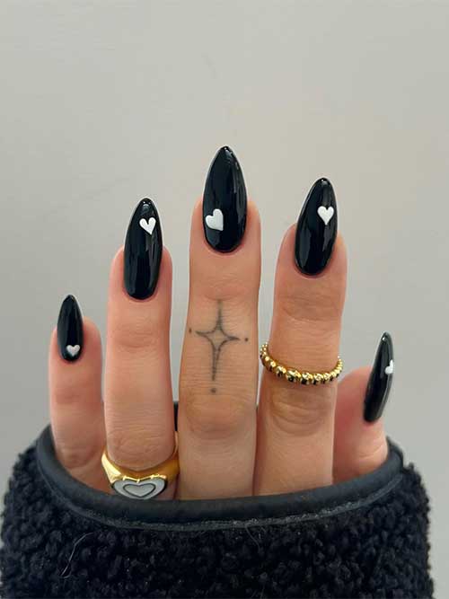 Almond-shaped simple black Valentine’s Day nails with a white heart shape on each nail Almond-shaped simple black Valentine’s Day nails with a white heart shape on each nail