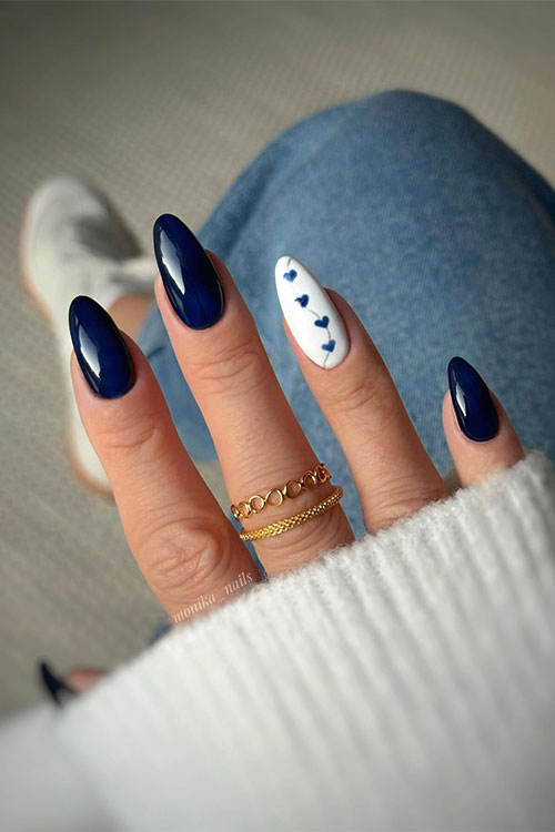 Dark navy blue almond-shaped nails with an accent white nail adorned with navy blue heart shapes
