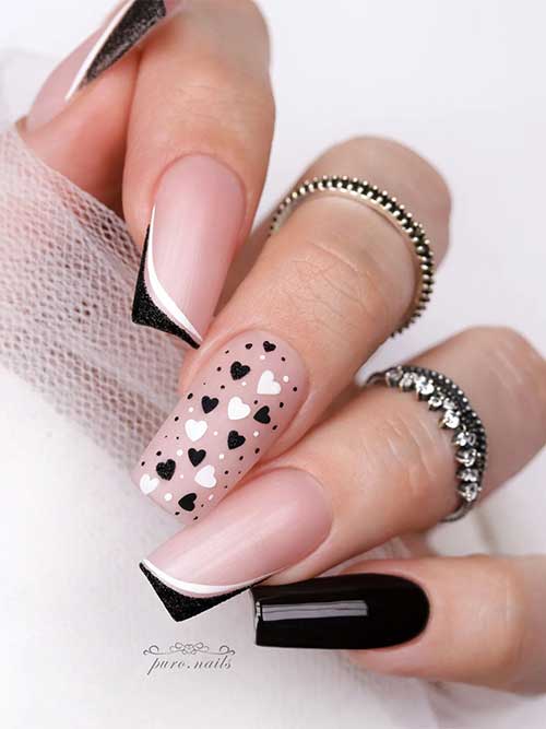 Double white and black diagonal French nails with an accent black nail, and a nude nail adorned with black and white hearts