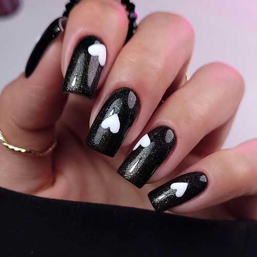 Glitter black Valentine’s Day nails adorned with a reversed white heart shape on each nail Glitter black Valentine’s Day nails adorned with a reversed white heart shape on each nail