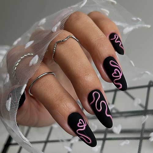 Long almond-shaped matte black Valentine’s Day nails with white and pink creative heart shape decorations on each nail