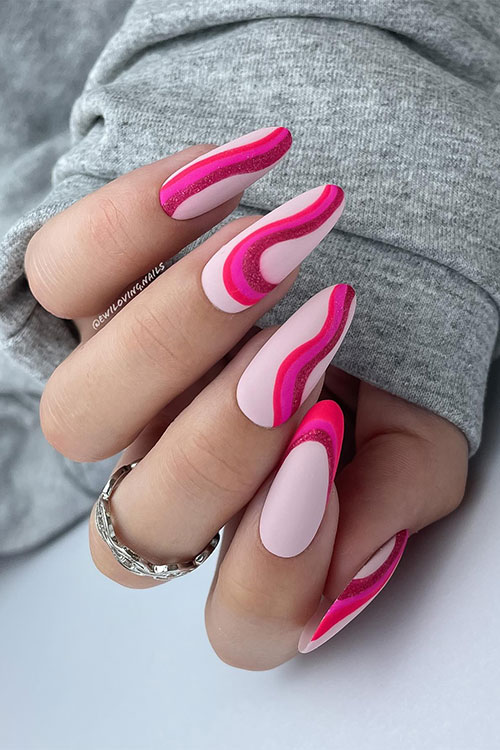 Long almond-shaped red, pink, and glitter red swirl nails over matte nude base color Long almond-shaped red, pink, and glitter red swirl nails over matte nude base color