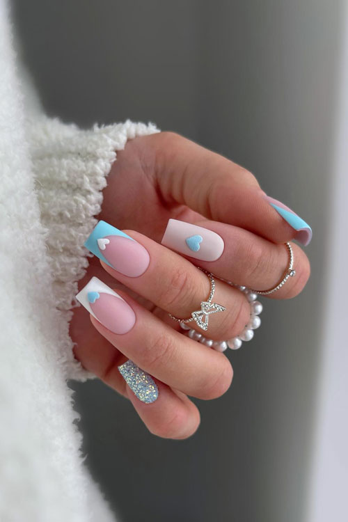 Matte French pastel Valentine’s Day nails feature white and light blue French nails adorned with hearts and glitter accent